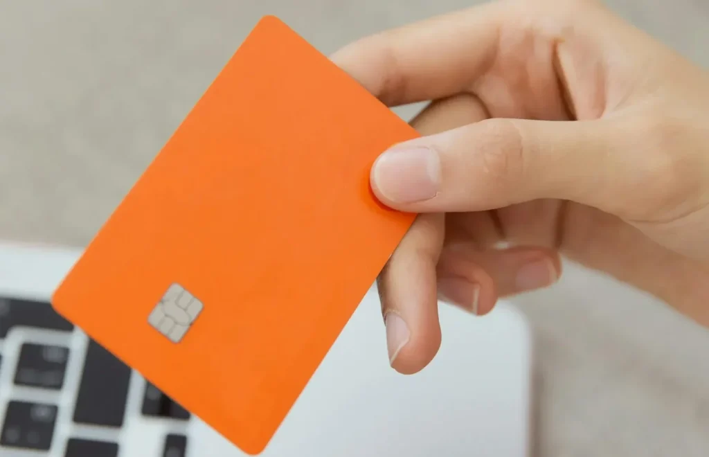 A hand holding an orange chip card above a laptop keyboard.